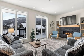 Een ruime woonkamer met een open haard, grote ramen en uitzicht op een besneeuwde berg.
