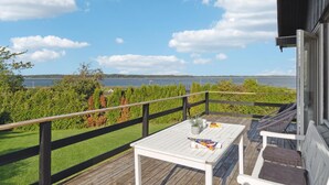 A wooden deck with a white table and chairs, overlooking a lake with a distant shoreline.