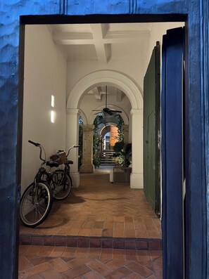 An indoor corridor with a bicycle, a ceiling fan, and a view of a building through an archway.