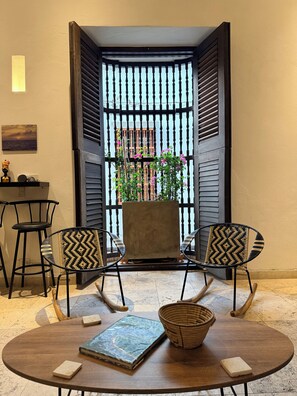 A room with a round table, two chairs, a small table with a chair, a decorative item, and a view through a window with a railing.