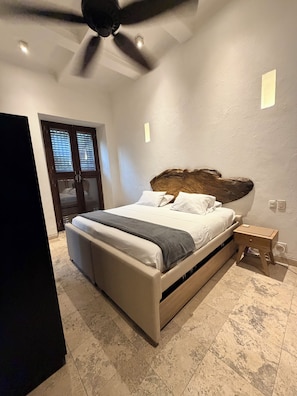 A bedroom with a bed, a bedside table, a ceiling fan, and a window with blinds.
