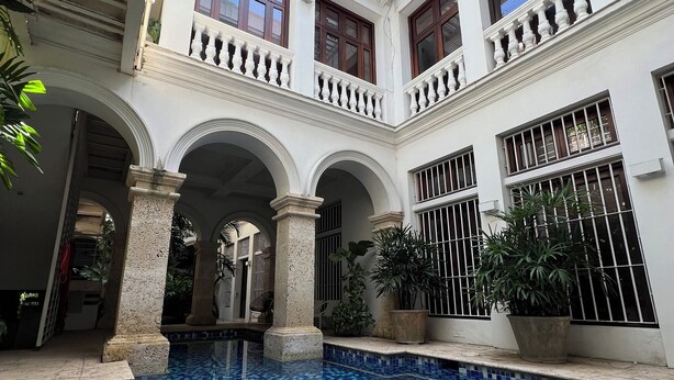 Un patio con piscina, columnas blancas y balcones con plantas.