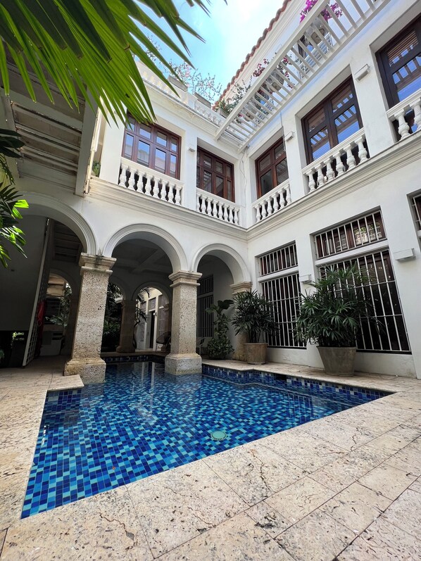 A courtyard with a pool, white columns, and balconies with plants.