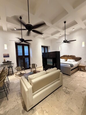 A modern living room with a sofa, a television, ceiling fans, and a dining area with chairs.