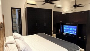 Un dormitorio moderno con cama, ventiladores de techo, televisión y armarios empotrados.