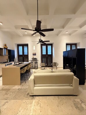 A modern kitchen with a central island, bar stools, and a ceiling fan.