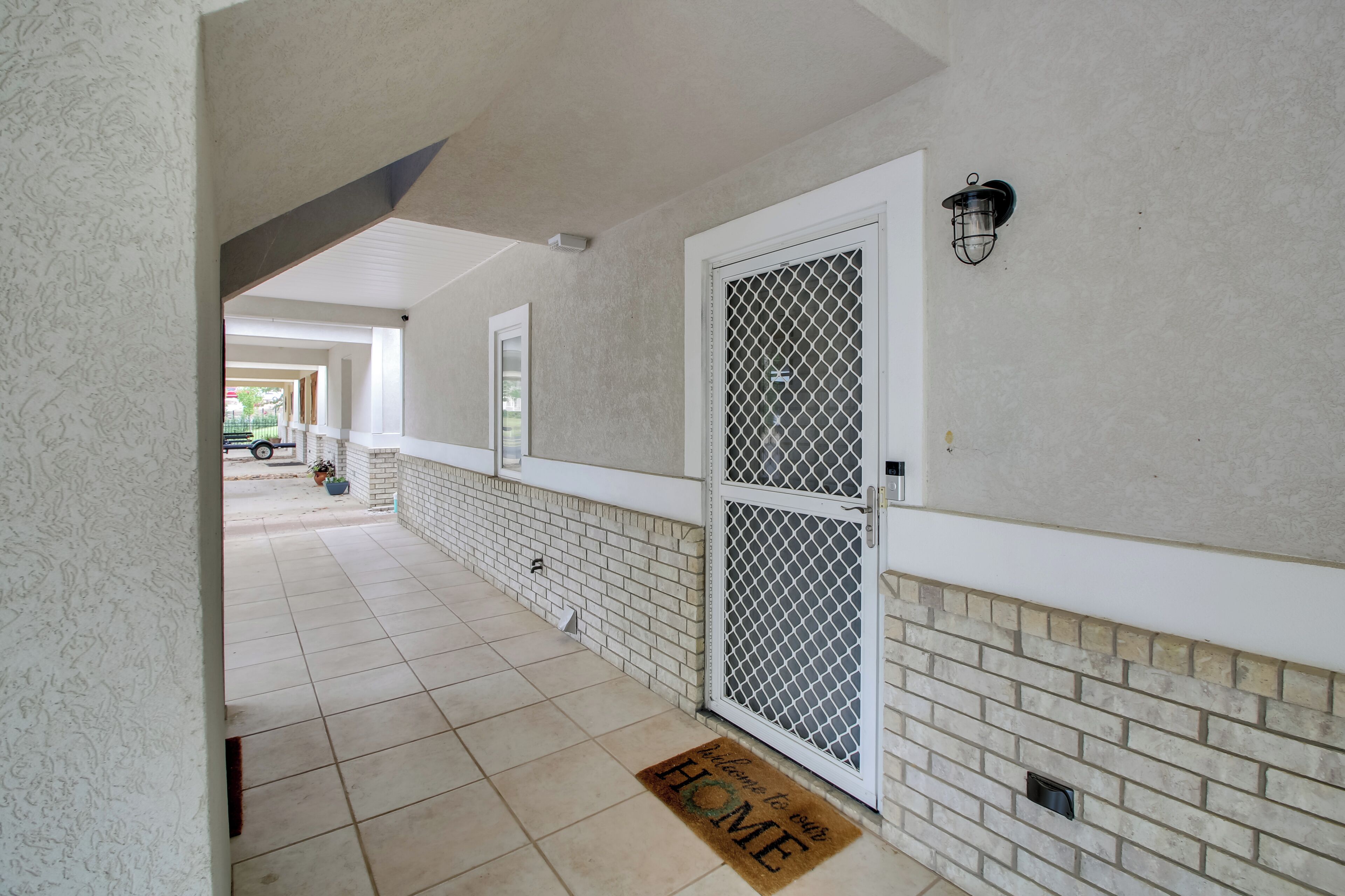 A covered walkway with a tiled floor, a metal gate, and a welcome mat.