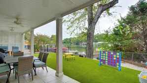 A covered patio with a table and chairs, a lawn, and a blue game board. - Hot Springs Retreat w/ Fireplace on Lake! (Hot Springs)