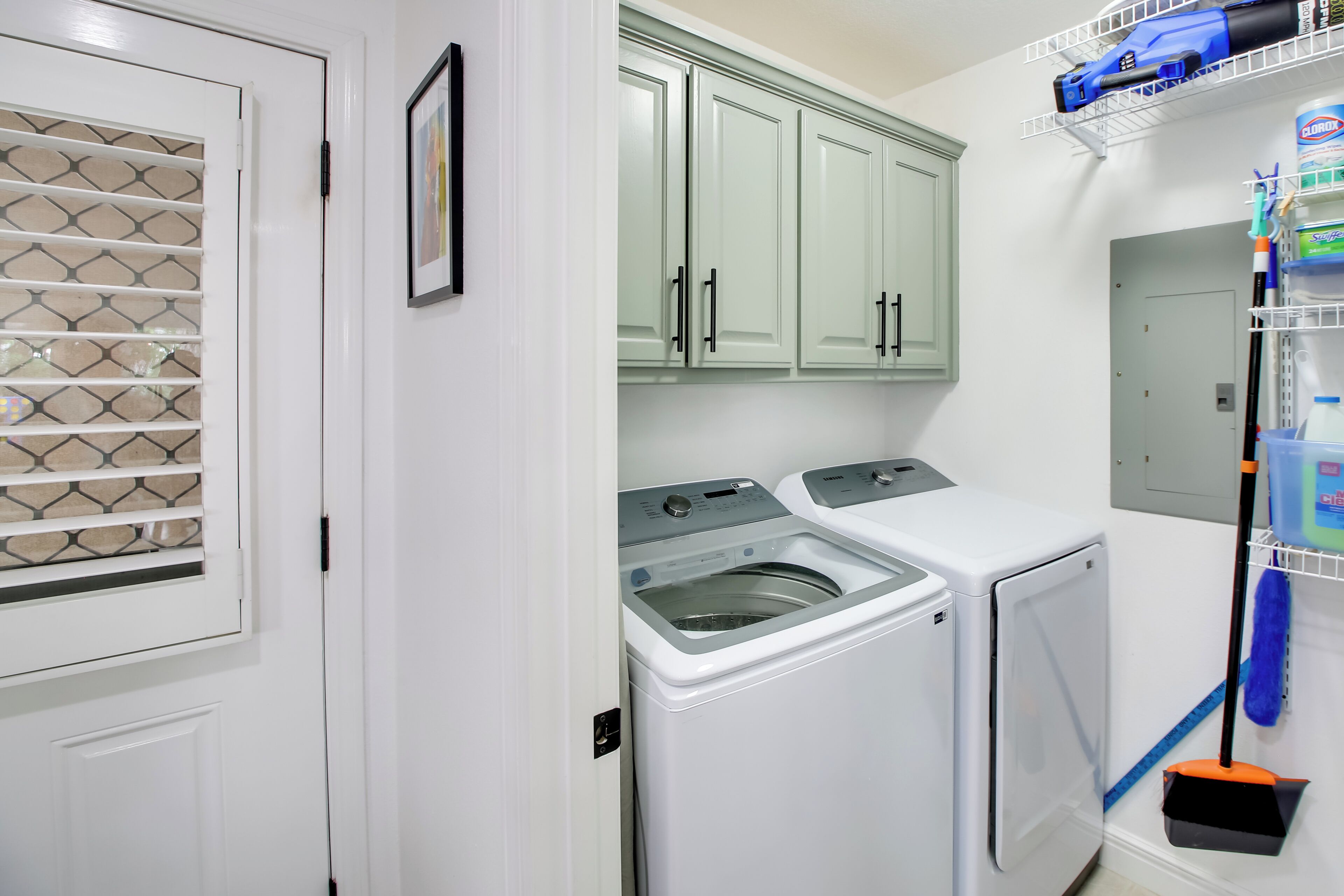 A laundry room with two washing machines, a drying rack, and a shelving unit with cleaning supplies.