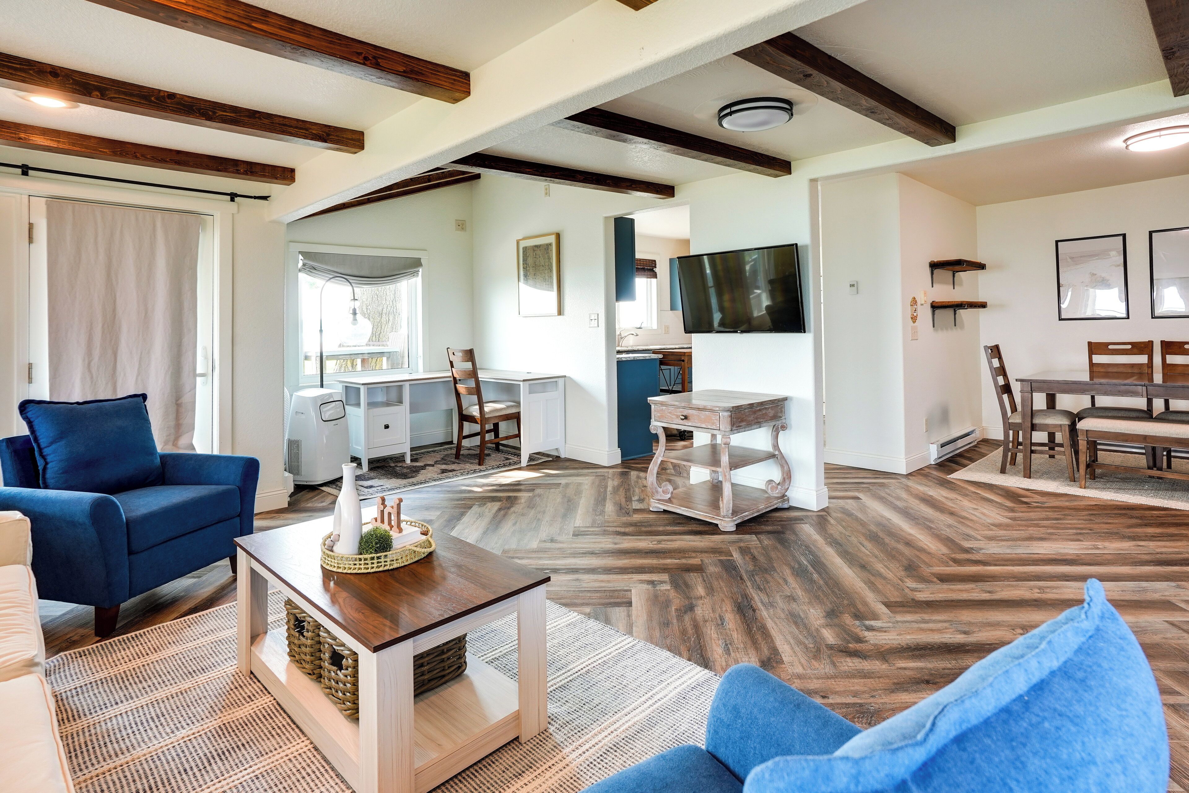 A spacious living room with a blue sofa, a wooden coffee table, and a television mounted on the wall.