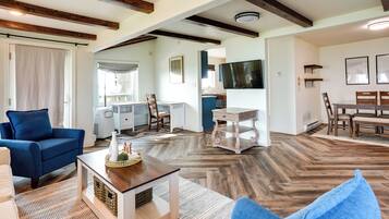 A spacious living room with a blue sofa, a wooden coffee table, and a television mounted on the wall.