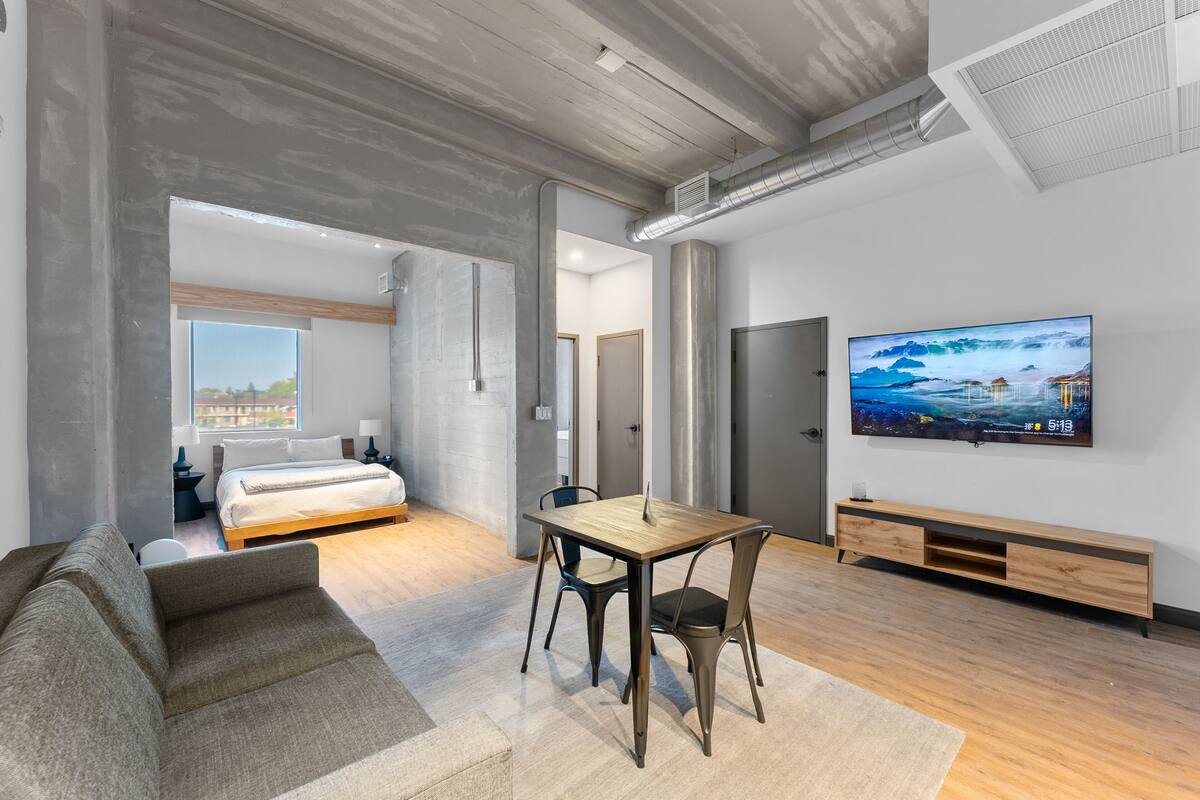A modern living room with a sofa, a wooden table, and a TV mounted on the wall.