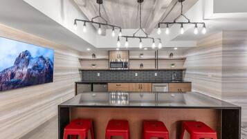 A modern kitchen with a large island, red bar stools, and a large flat-screen TV.