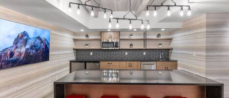 A modern kitchen with a large island, red bar stools, and a large flat-screen TV.