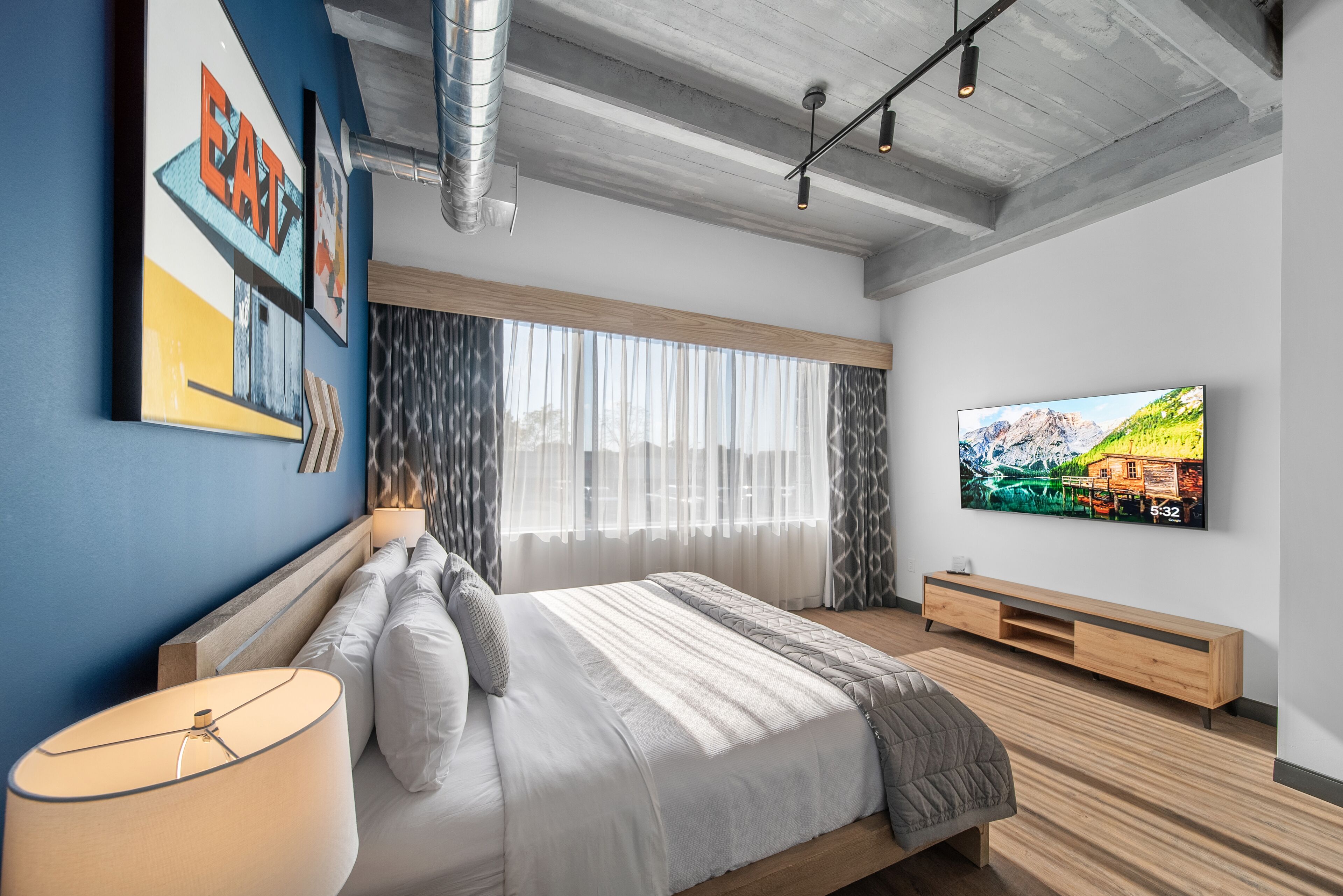 Un dormitorio moderno con una cama grande, un televisor montado en la pared y un banco de madera.