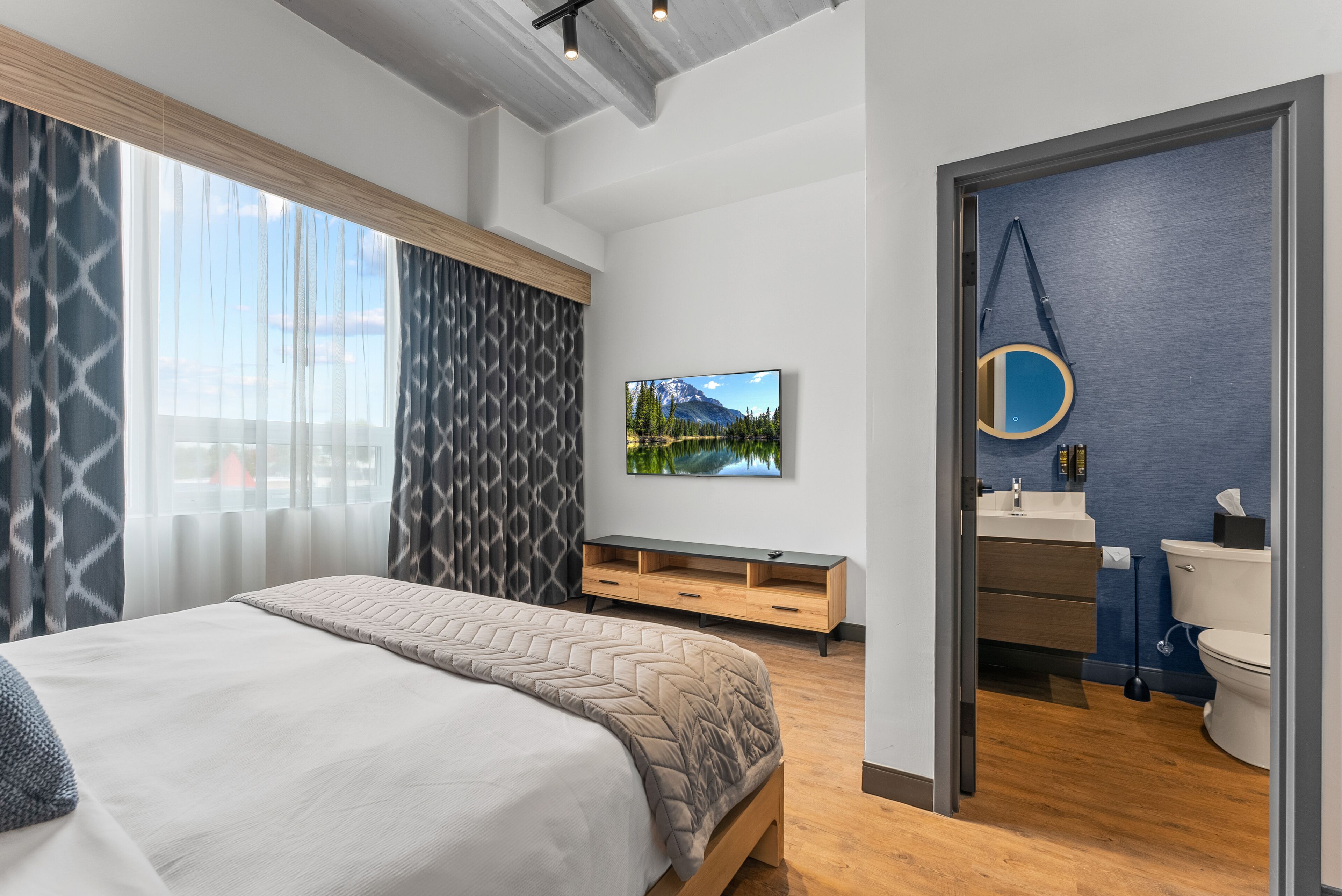 Un dormitorio moderno con una cama grande, un televisor, un banco de madera y un baño con una pared azul de acento.