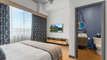 Un dormitorio moderno con una cama grande, un televisor, un banco de madera y un baño con una pared azul de acento.