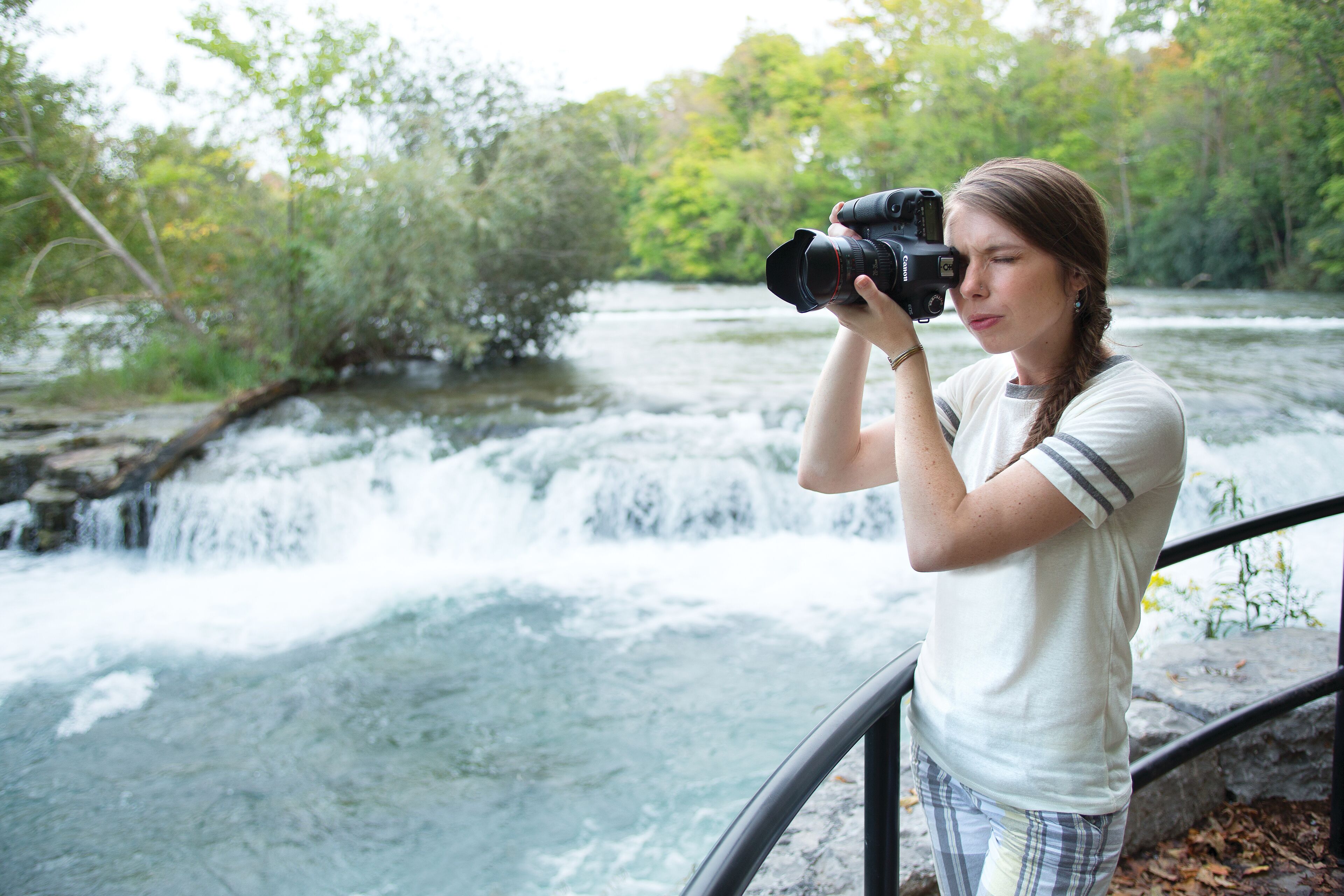 Eine Person fotografiert mit einer Kamera einen Wasserfall.