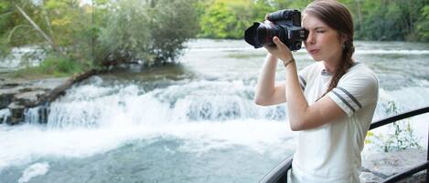 A person taking a photo with a camera near a waterfall.