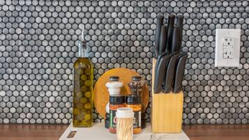 Una encimera de cocina con tabla de cortar, una botella de aceite de oliva, frascos de especias y un bloque de cuchillos.