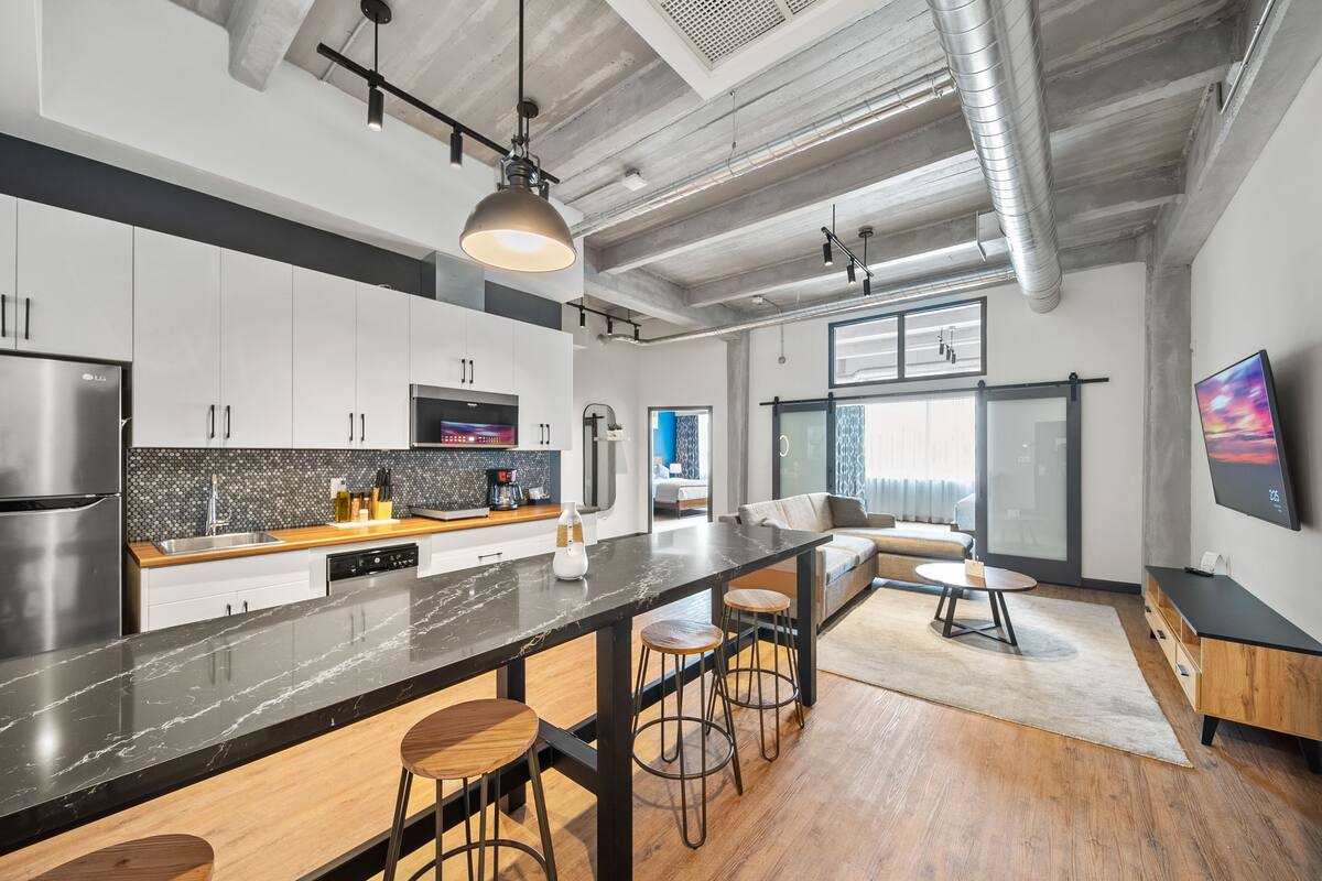 A modern kitchen with a long island, bar stools, and a large TV on the wall.