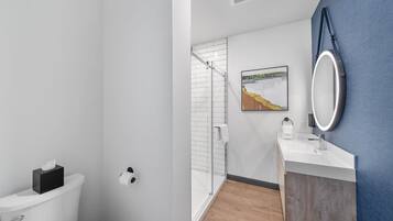Un baño moderno con inodoro, ducha, lavabo y espejo.