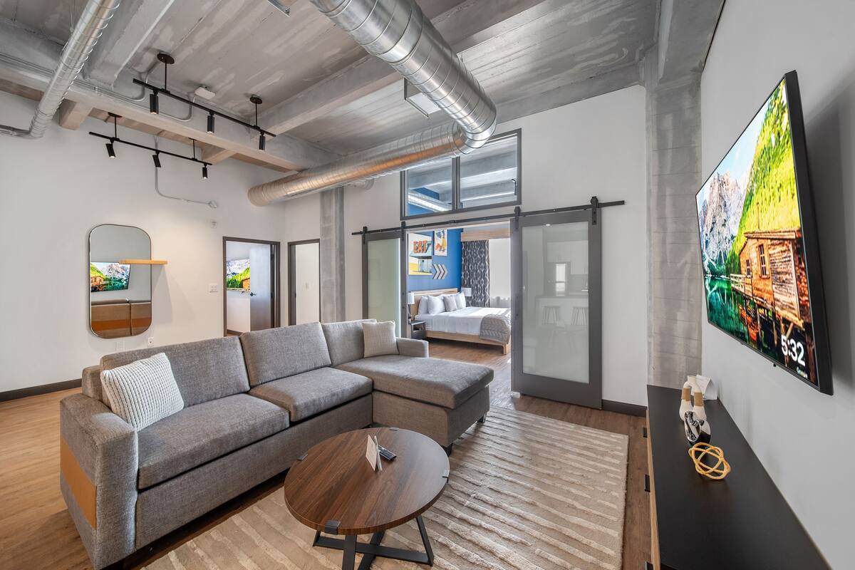 A modern living room with a sectional sofa, a coffee table, and a flat-screen TV mounted on the wall.