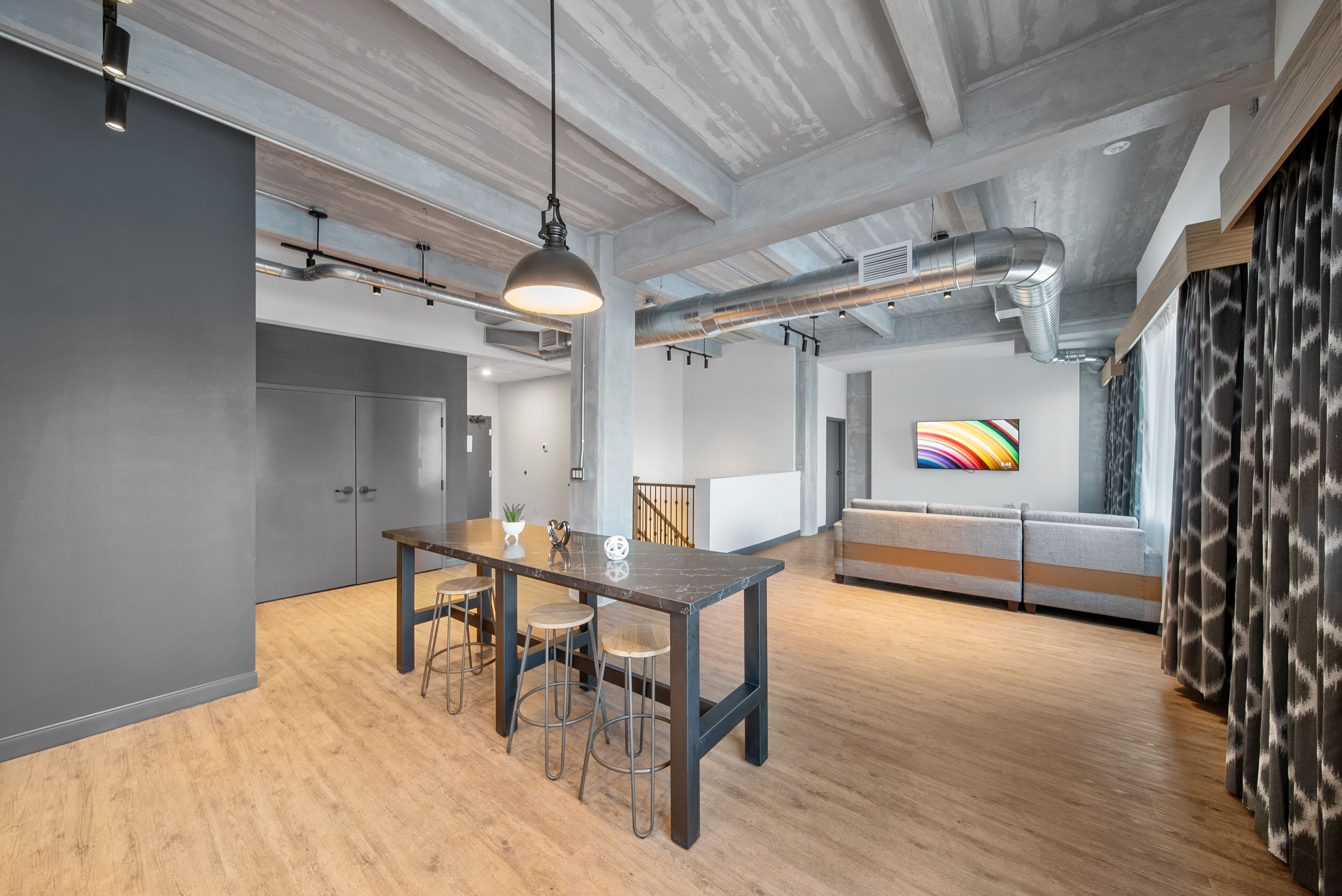 Un espace de bureau moderne avec une table et des chaises en bois, un luminaire suspendu et une peinture abstraite aux couleurs vives accrochée au mur.