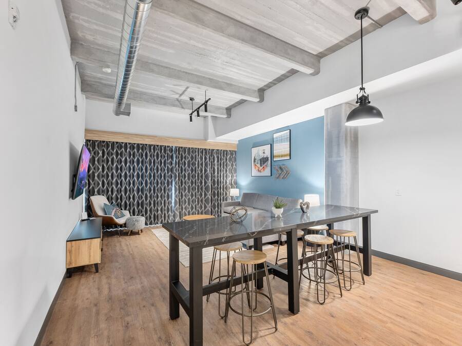 A modern kitchen with a marble countertop, bar stools, and a hanging pendant light.