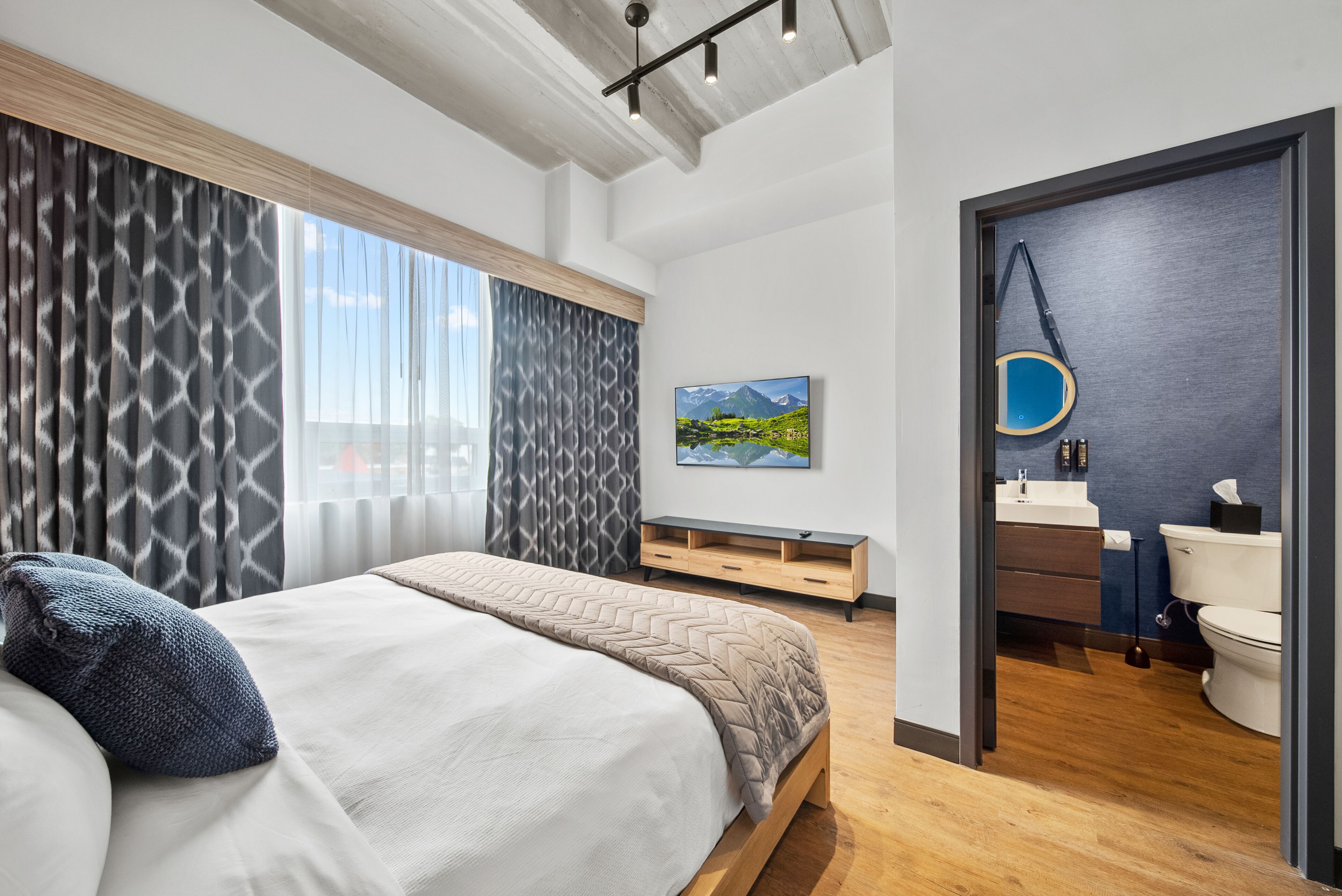 Une chambre à coucher moderne avec un lit, une vue sur la salle de bain et un tableau accroché au mur.