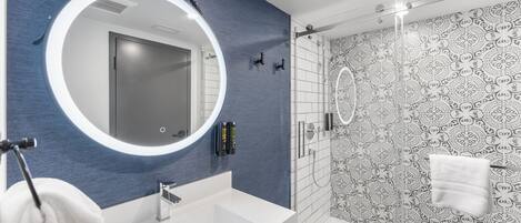 Un baño moderno con un espejo grande, un lavamanos blanco y una ducha con paredes de vidrio.