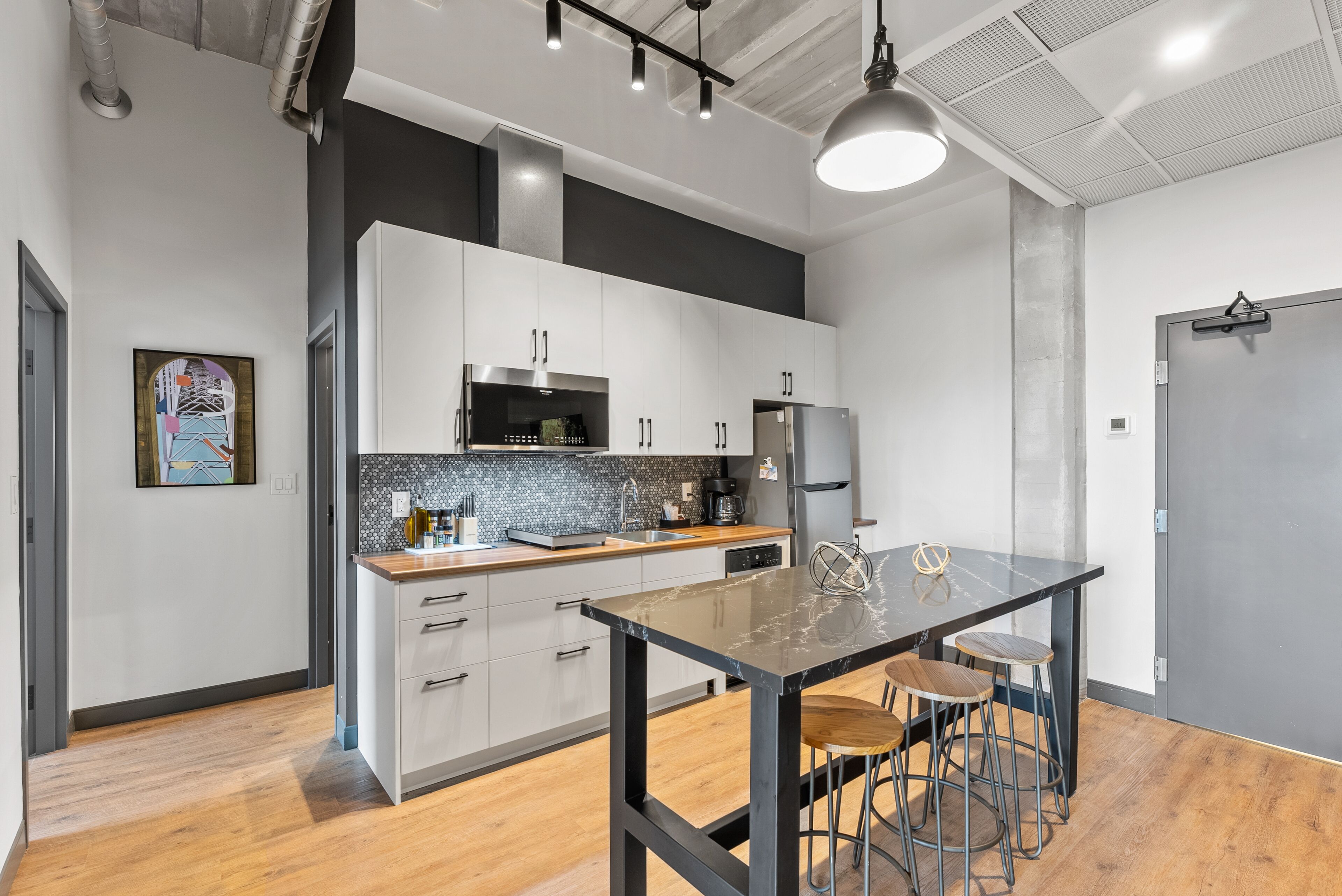 A modern kitchen with white cabinets, a black countertop, and a marble island with stools.