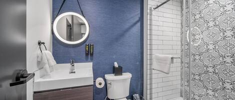 A modern bathroom with a blue accent wall, a round mirror, a white sink, and a glass shower enclosure.