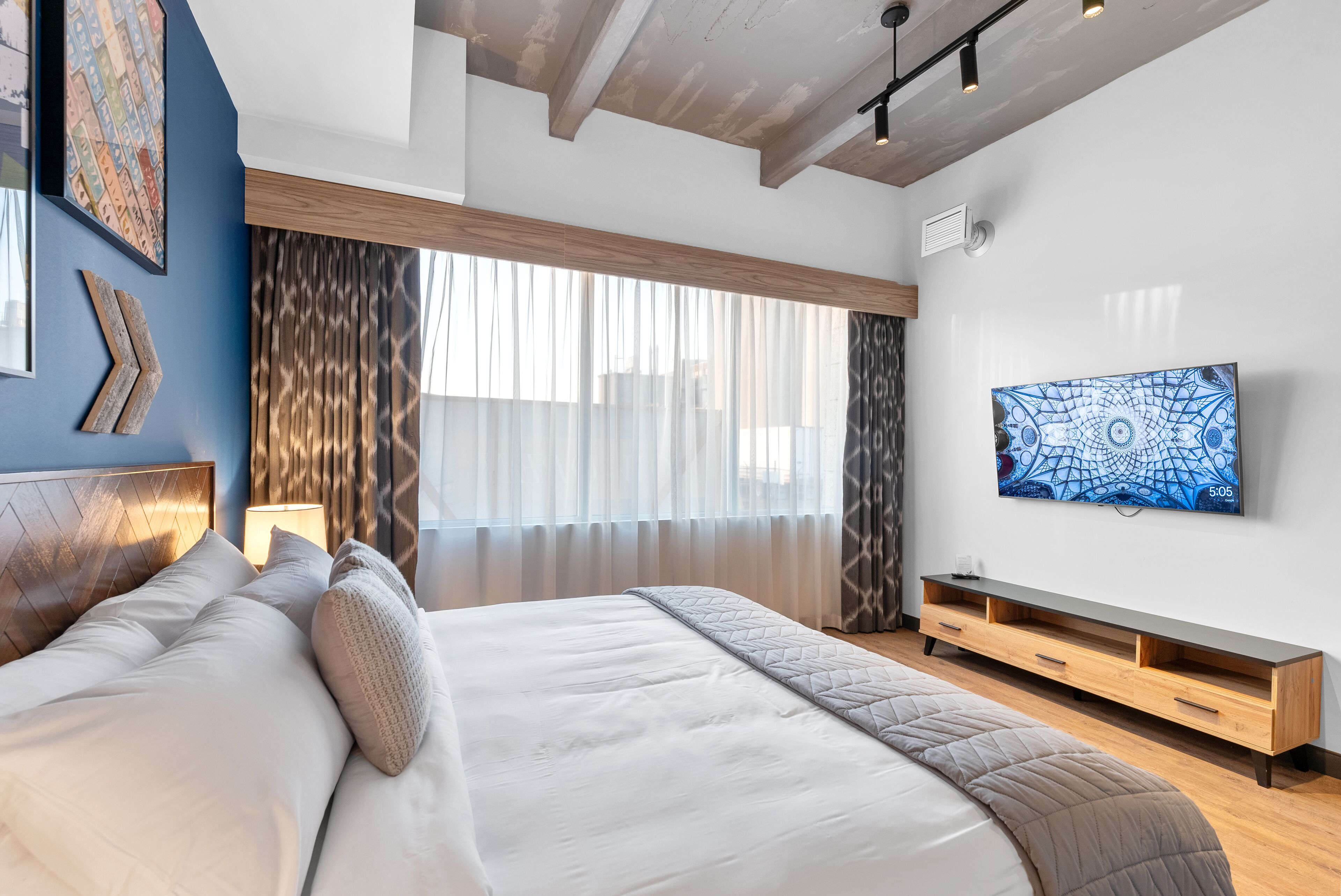 A modern bedroom with a large bed, a TV on the wall, and a wooden bench.