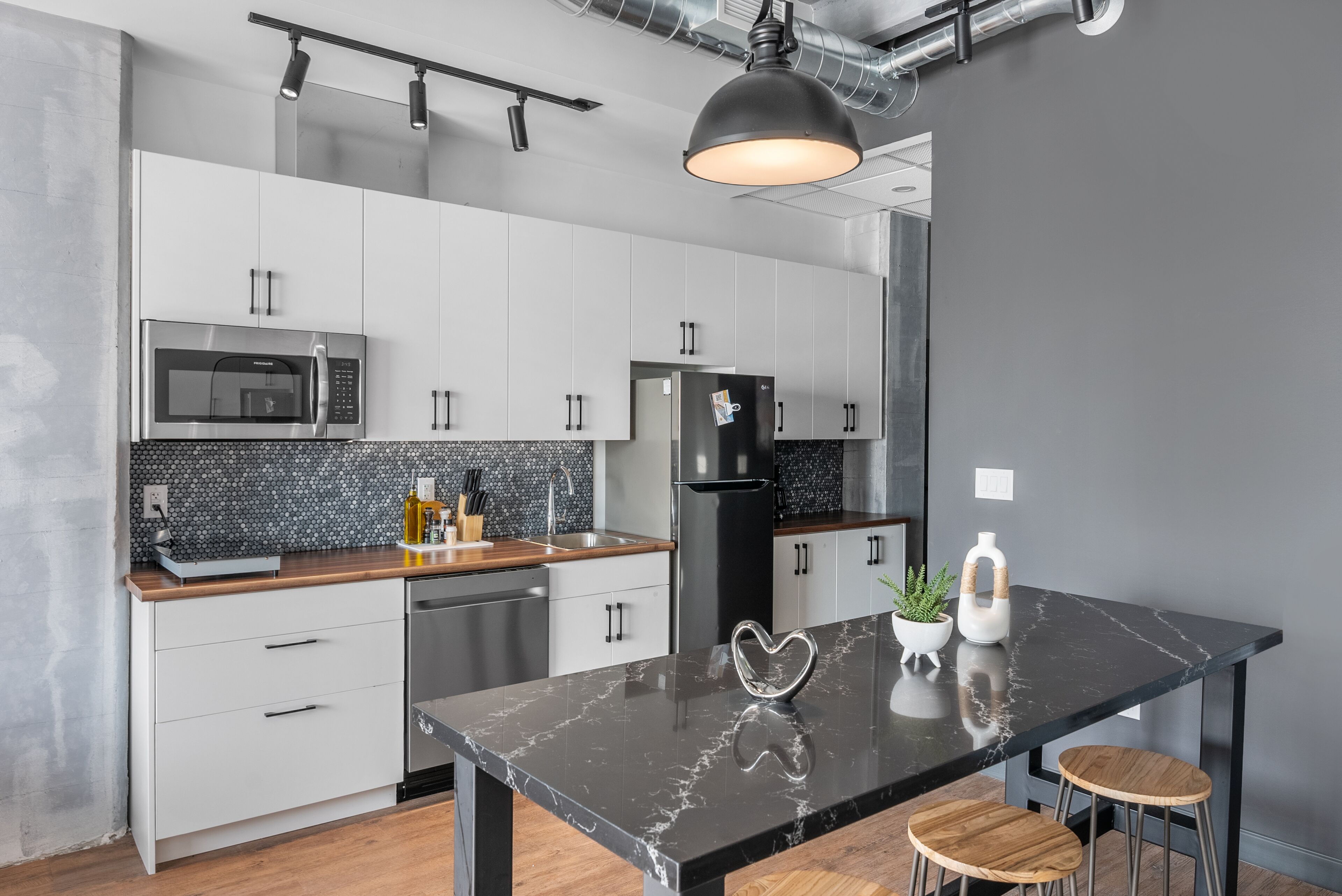 A modern kitchen with white cabinets, a black marble island, stainless steel appliances, and a pendant light.