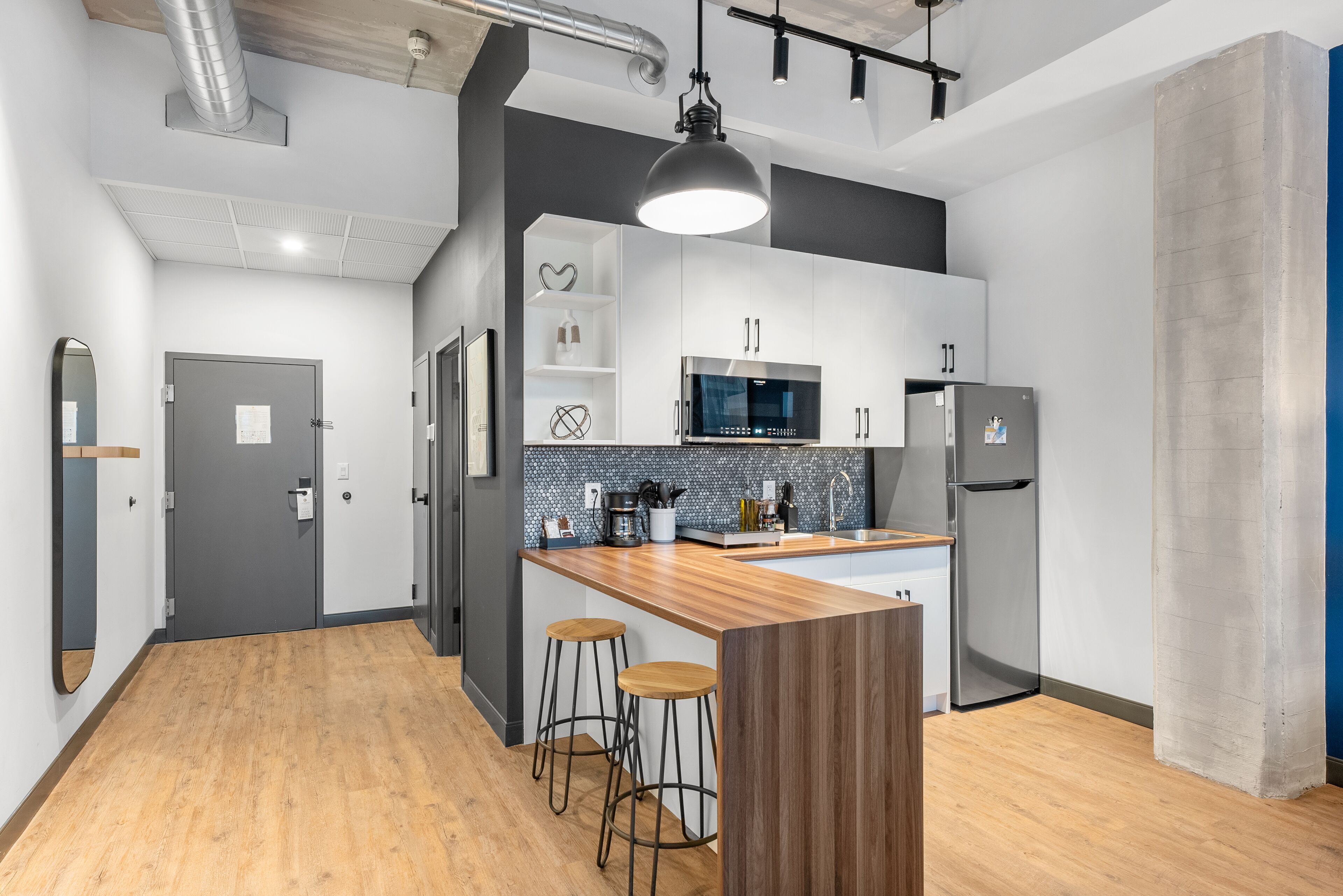 Cozinha moderna com ilha de madeira, banquetas, micro-ondas e geladeira.