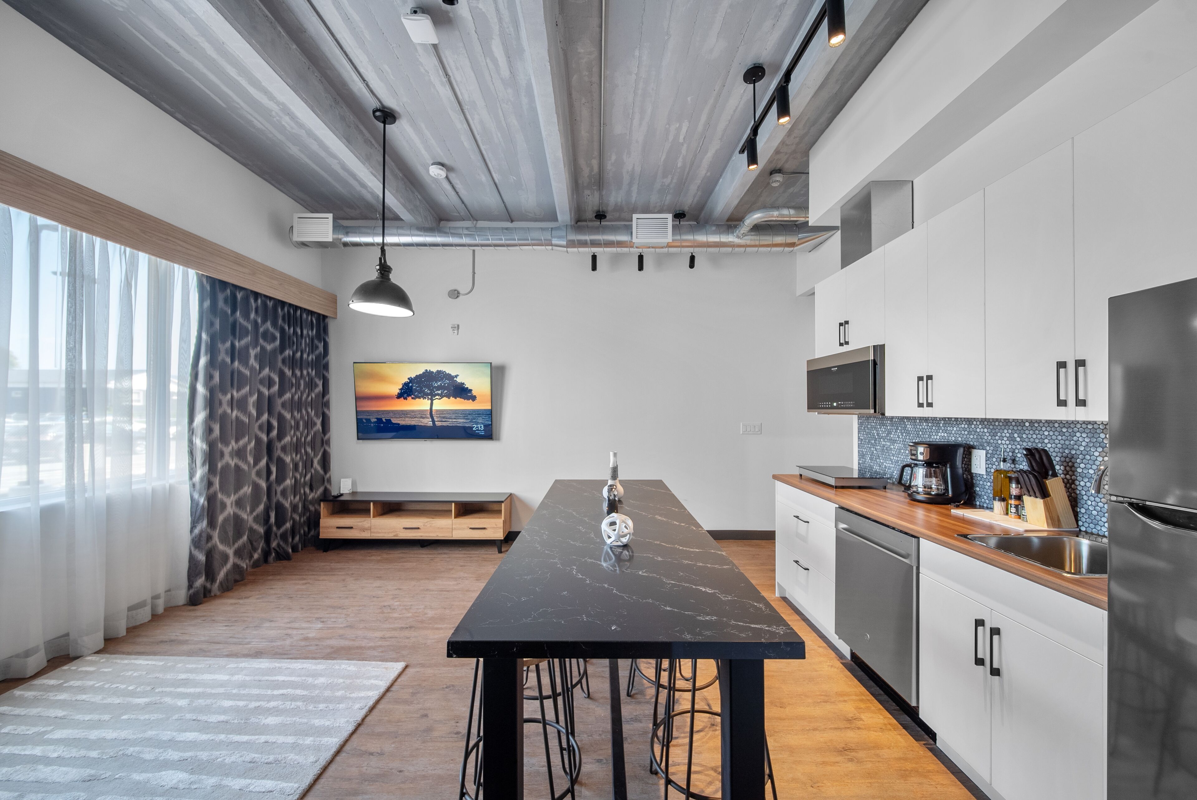 A modern kitchen with a marble countertop, stainless steel appliances, and a wooden floor.