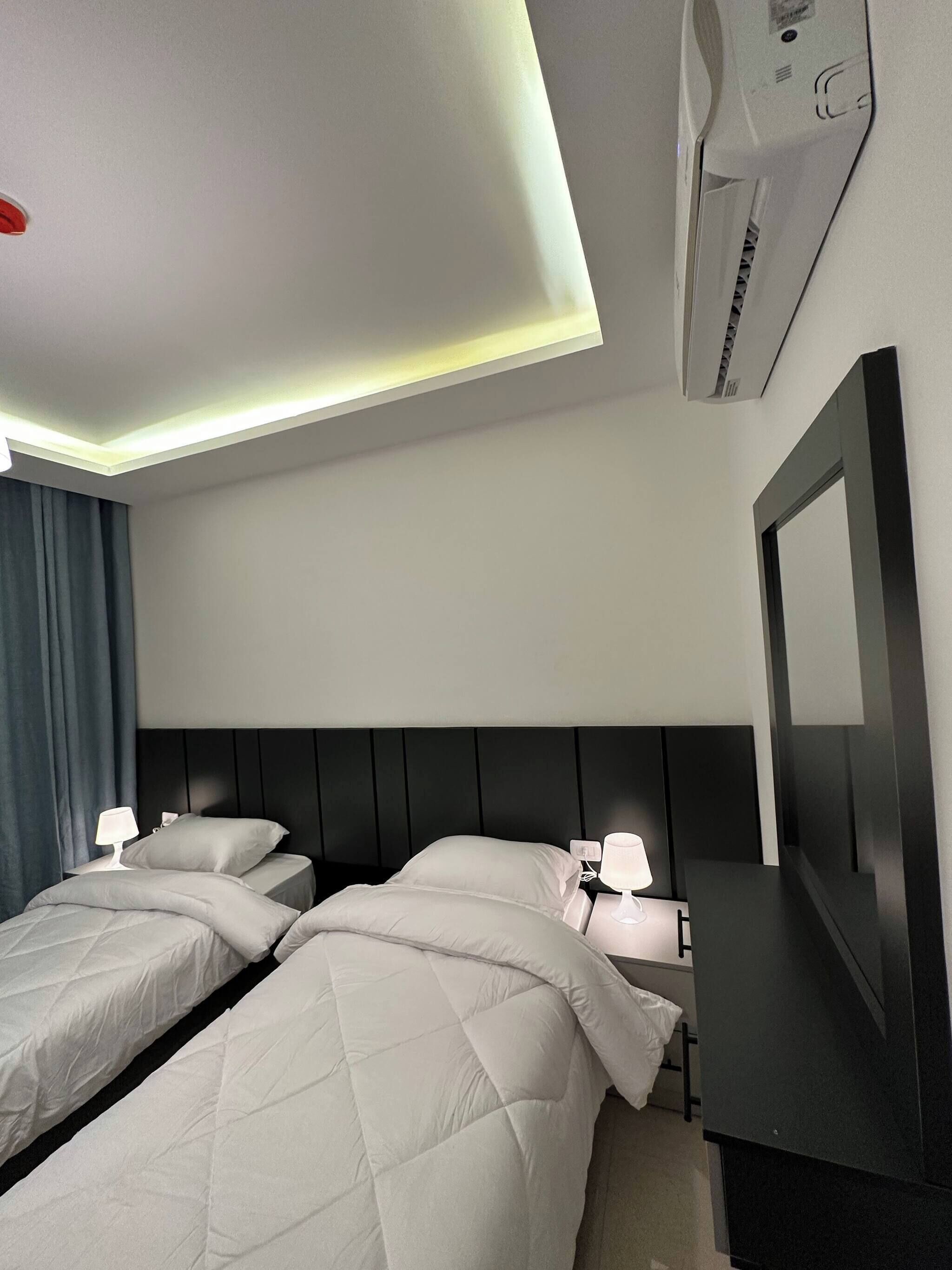 A hotel room with two beds, a ceiling light, an air conditioning unit, and a wall-mounted TV.