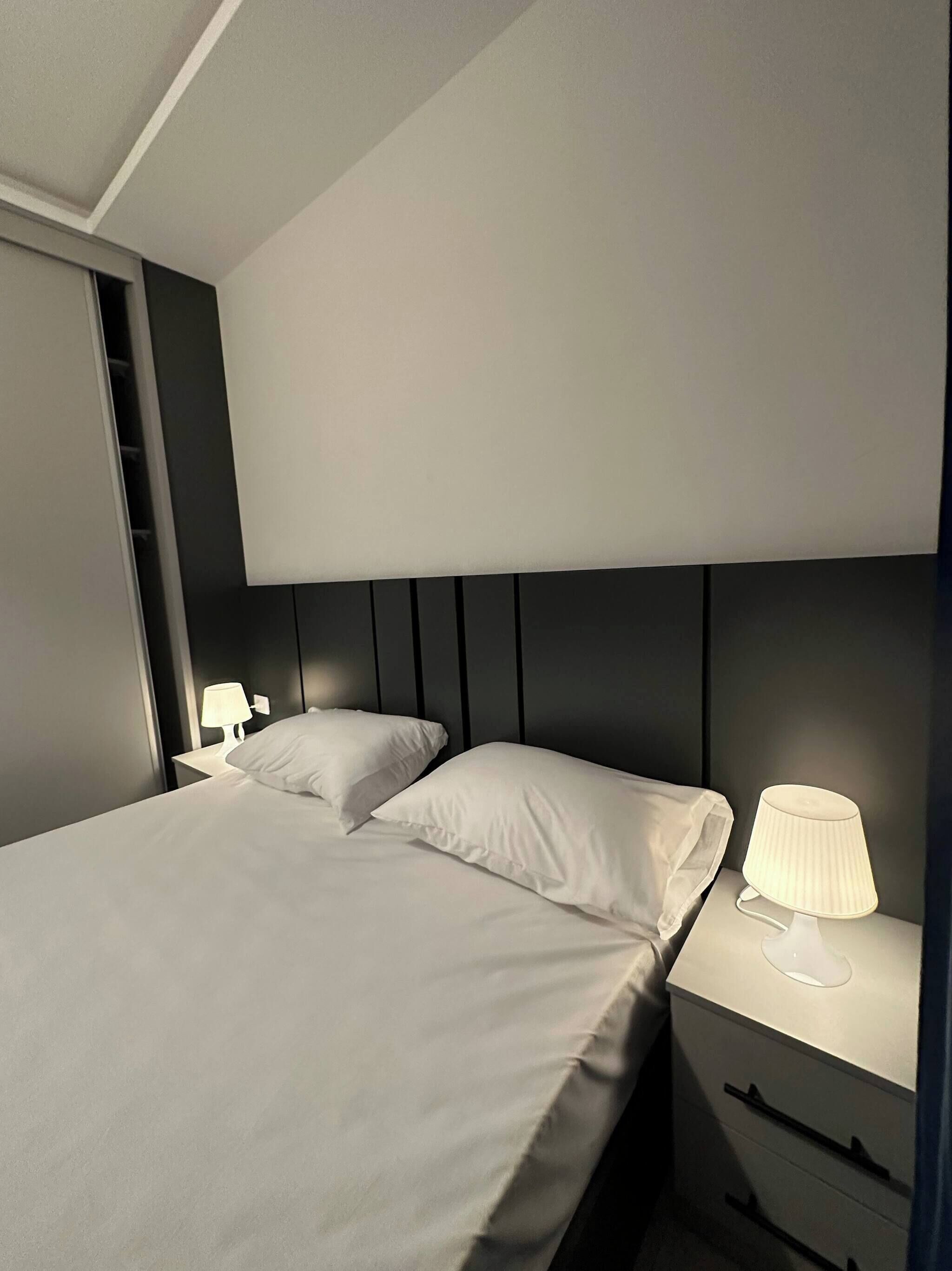Um quarto moderno com uma cama, duas mesas de cabeceira e uma mesinha de apoio.
