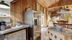 Una cocina con paredes de madera, un refrigerador de acero inoxidable, una mesa de madera con una lámpara y un piso de baldosas.