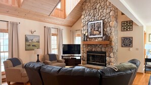 A cozy living room with a stone fireplace, a large flat-screen TV, and a comfortable seating area. - Longwood Hideaway - A Warm, Elegant Retreat for Rest & Restoration (Galena)