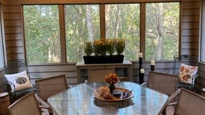 A covered outdoor dining area with a table and chairs, surrounded by large windows offering a view of trees. - Longwood Hideaway - A Warm, Elegant Retreat for Rest & Restoration (Galena)