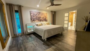 A modern bedroom with a large bed, a bedside table with a built-in light, a ceiling fan, and a large window with curtains. - Little Ranches Retreat in the Heart of Equestrian Community  (Wellington)