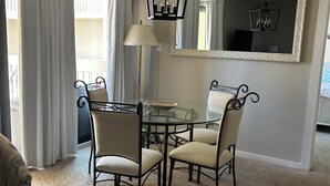 Een eetgedeelte met een glazen tafel en vier stoelen, een vloerlamp, een spiegel en een plafondlamp.