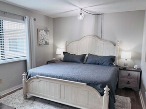 A bedroom with a bed, bedside lamps, a nightstand, a wall clock, and a window with blinds.
