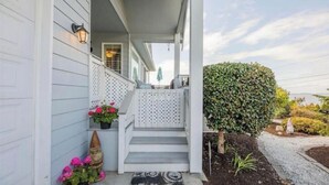 Een wit huis met een veranda, trappen en een haag.