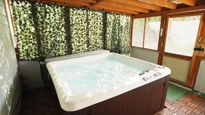 Een bubbelbad in een kamer met houten balken en een groene wand begroeid met planten.