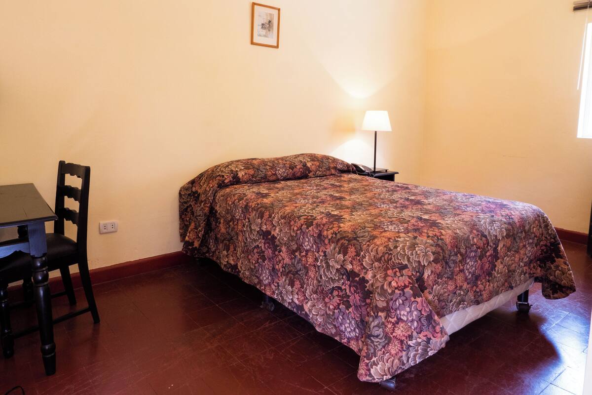 Une chambre à coucher avec un lit, une chaise, une table de chevet et une lampe.