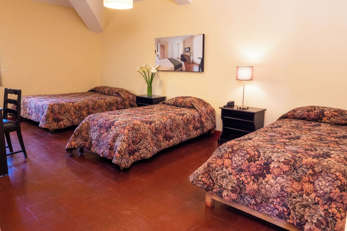 Une chambre d’hôtel avec trois lits, un bureau, une chaise et un miroir au mur.