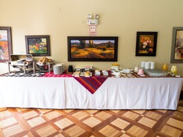 A buffet table with various food items and beverages, a clock, and emergency exit signs on the wall.